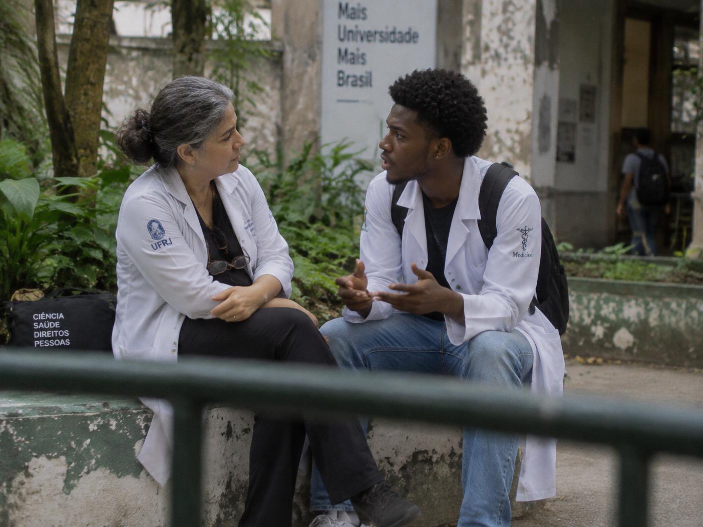 Uma médica mais experiente escuta um estudante durante uma conversa no pátio da universidade